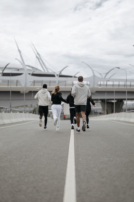 A group of people jogging together on an empty urban road next to a modern bridge.