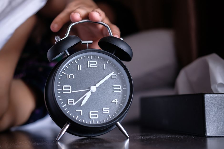 Test de chronotype : ce que votre sommeil mesure vraiment A hand reaches out to turn off an analogue alarm clock in the early morning.