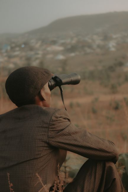 A man in a hat observing the distance with binoculars outdoors.