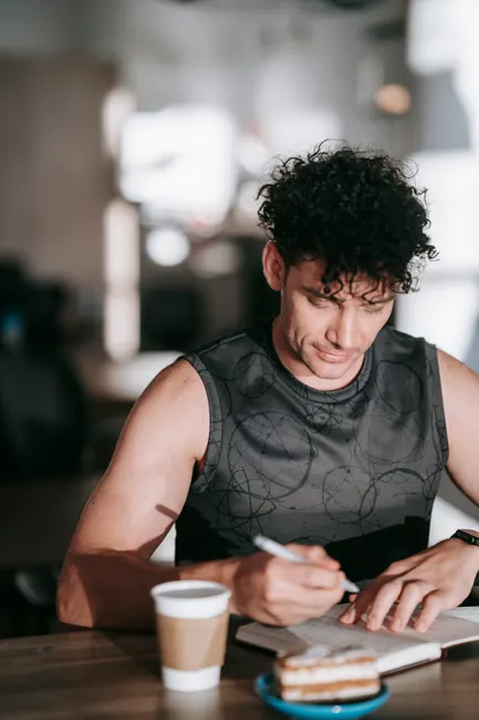 A man in activewear writing in a journal, enjoying coffee indoors.