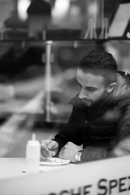 A man is seen eating alone in a restaurant setting, captured in black and white.