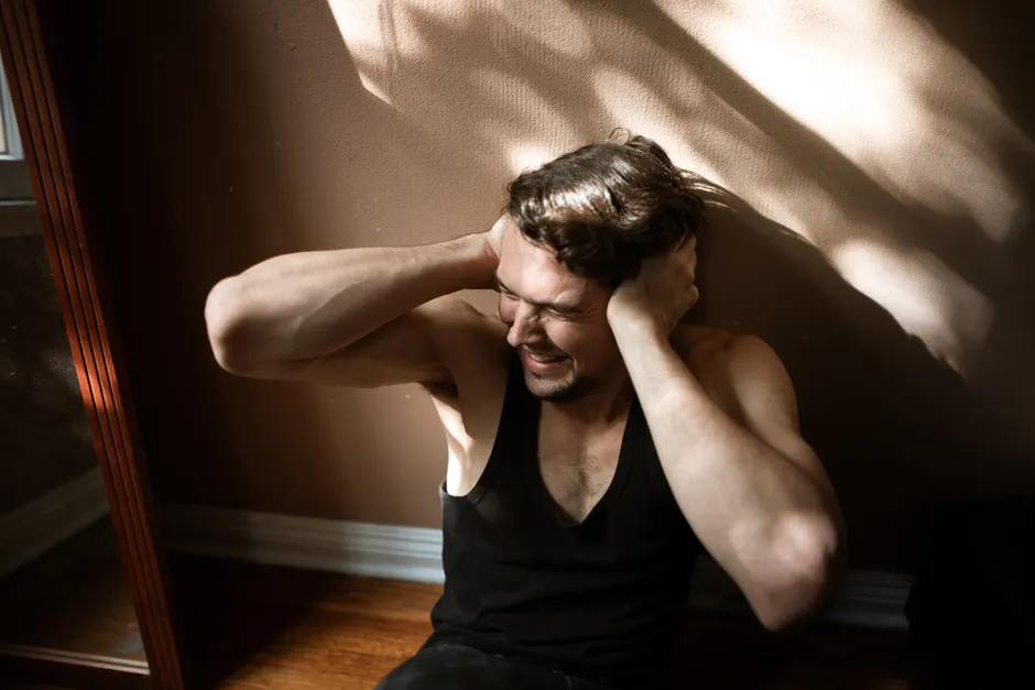Hypersensibilité auditive et autisme : comprendre ce que le bruit change A man sitting on the floor indoors, showing signs of stress by covering his ears.