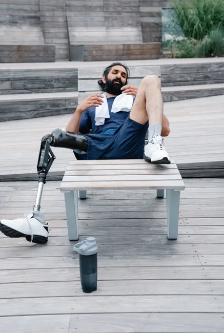 A man with a prosthetic leg relaxing outdoors on a wooden deck, embodying rest and resilience.