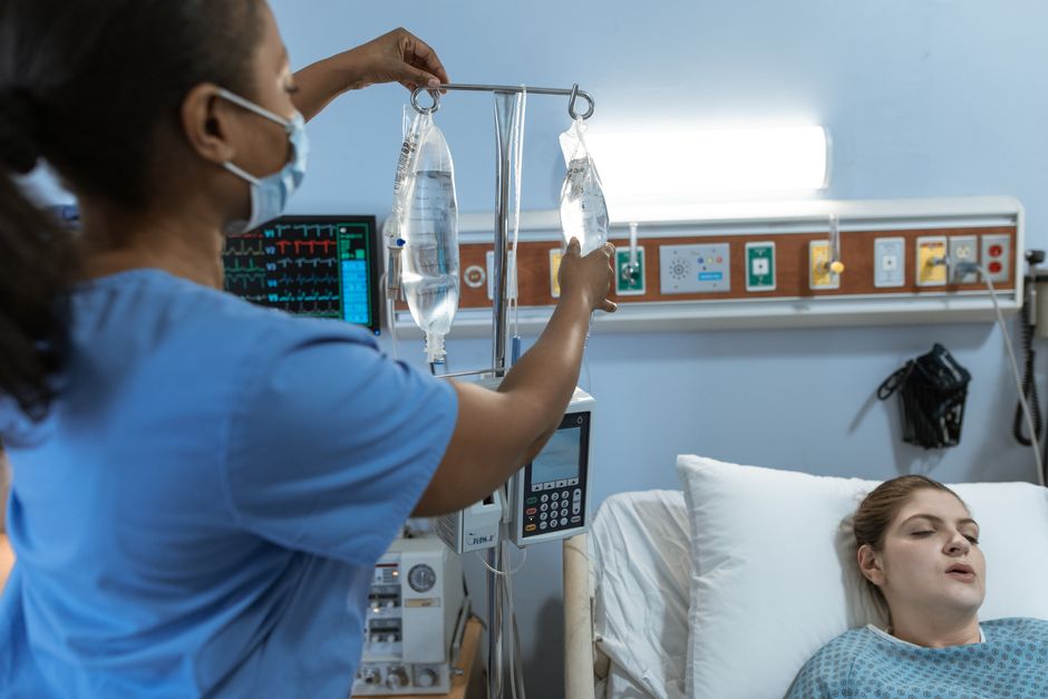 Fatigue compassionnelle des soignants : quand aider épuise A nurse in a hospital setting adjusts an IV drip for a patient lying in bed, showcasing medical care.