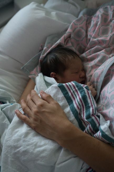 A peaceful scene of a mother cuddling her sleeping newborn in a hospital setting.