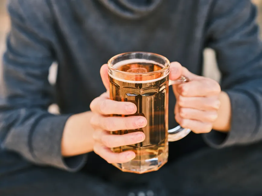 Addiction à l’alcool : douleur, isolement et vulnérabilité A person holding a clear glass mug filled with beer, focus on the hands and drink.