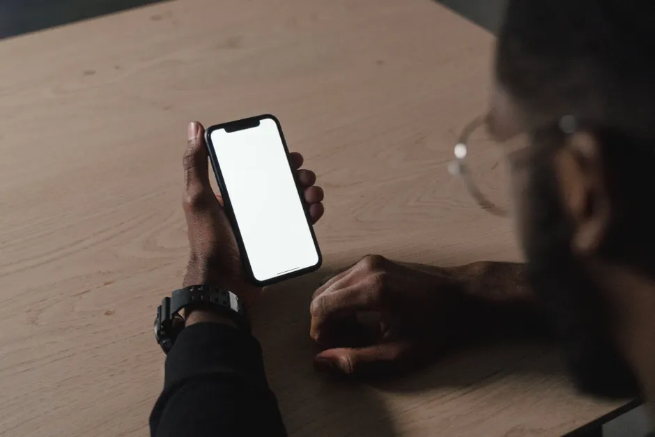Contrôle coercitif dans le couple : quand l’emprise rétrécit la vie A person holds a smartphone with a blank screen in a dimly lit room, emphasizing technology use.