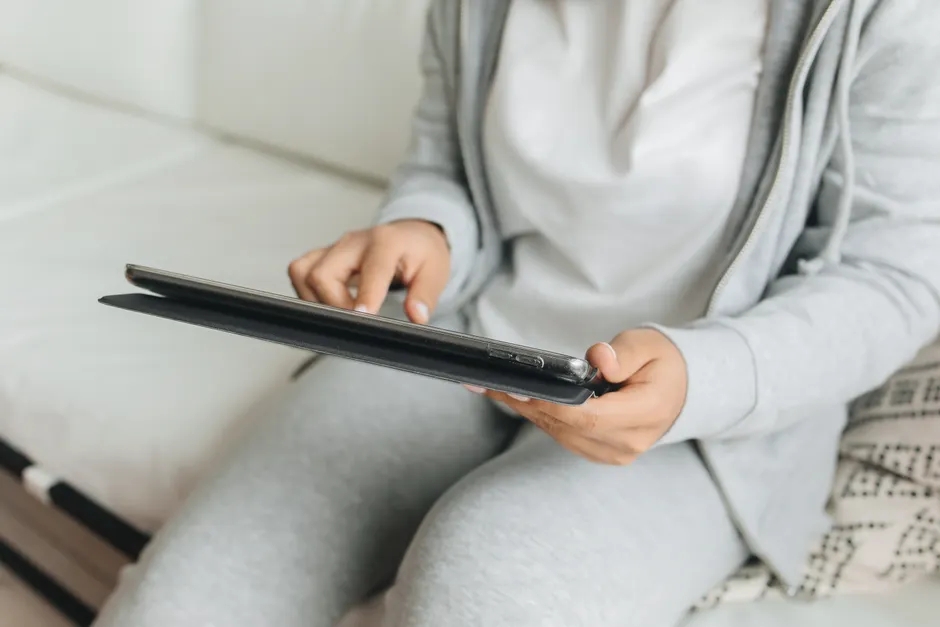 Communication alternative et augmentée : choisir un tableau qui laisse parler la personne A person in casual wear using a tablet while sitting indoors, focusing on hands and device.