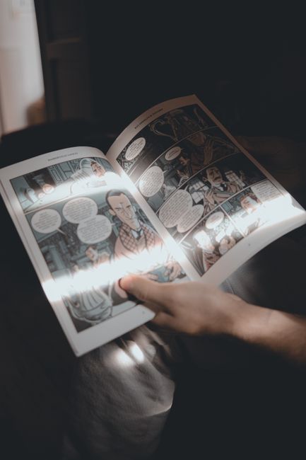 A person reading a comic book illuminated by soft sunlight indoors.