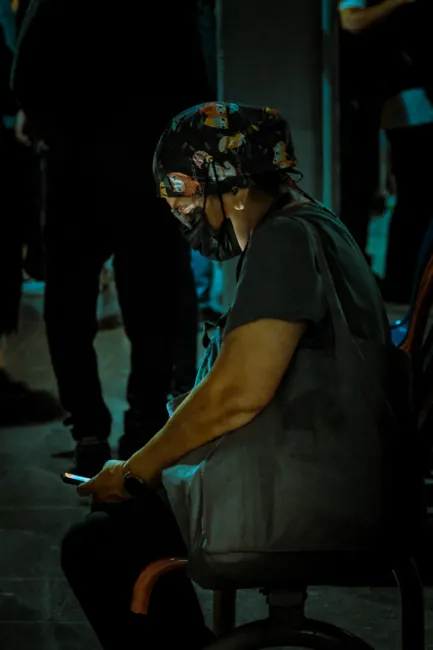 A person sits quietly at night in an urban setting, absorbed in their phone.
