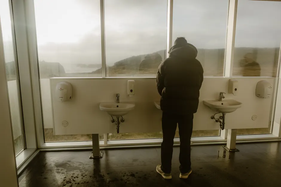 Peur de faire caca en public : TOC, phobie ou anxiété sociale? A person stands in a modern restroom with large windows offering a scenic, misty view outside.
