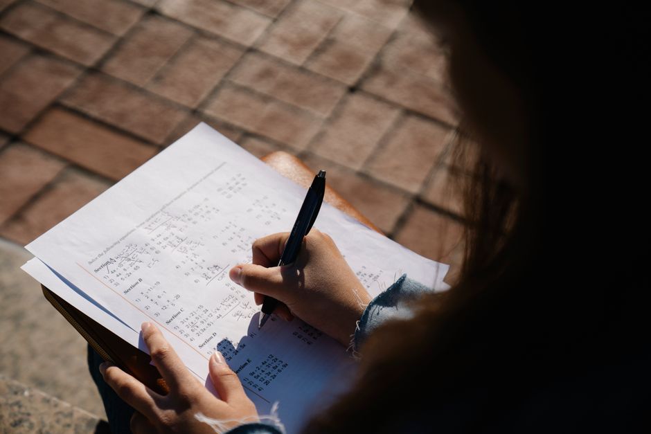TCC et anxiété : ce que la thérapie change dans la vie quotidienne A person writing calculations on a mathematical worksheet with a pen outdoors.