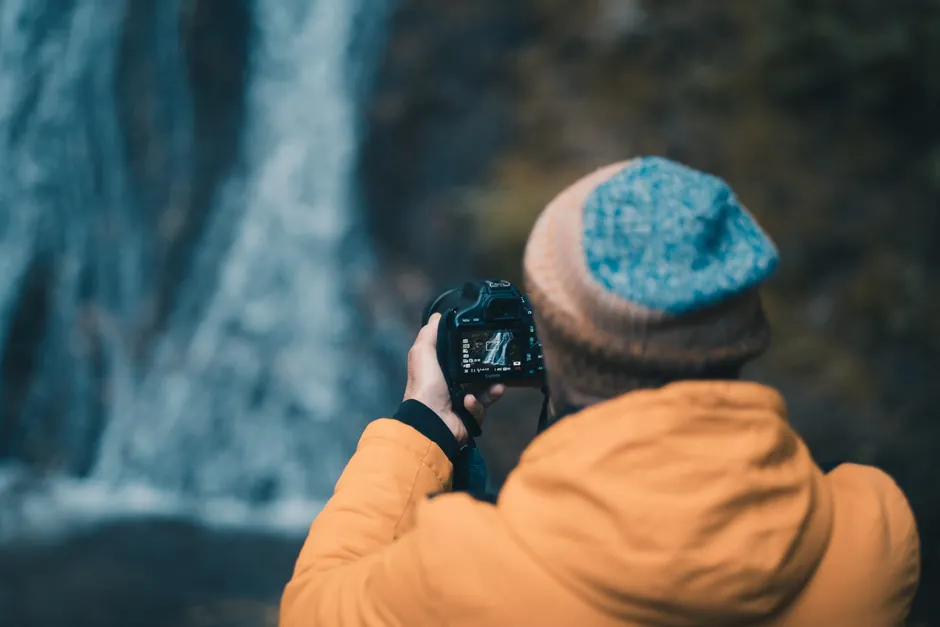Bonheur : quatre travaux récents, de la nature aux transitions de vie A photographer in a jacket and cap captures a waterfall in nature.