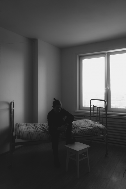 A silhouette of a person sitting on a bed in a minimalist room with soft natural light.