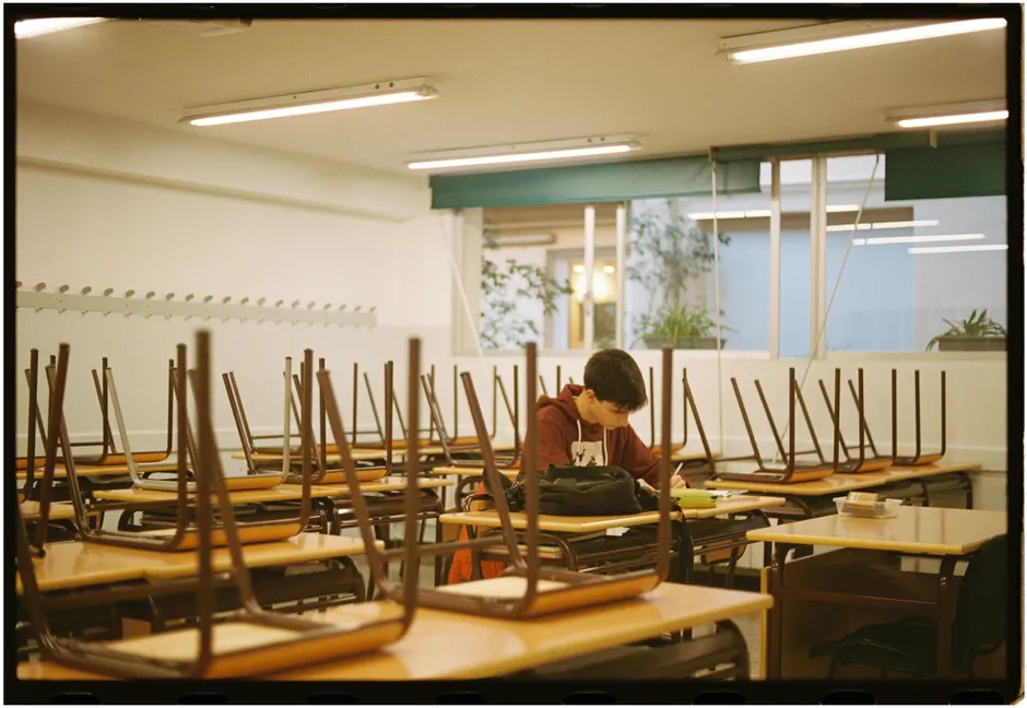 A student diligently studies alone in a quiet, empty classroom filled with chairs and desks.