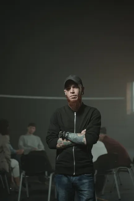 A tattooed man leads a diverse support group in a calm setting.