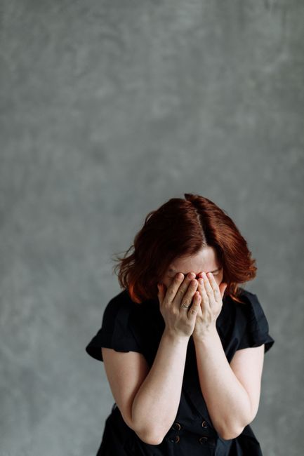 A woman feeling distressed and emotional, covering her face, against a textured concrete background, conveying themes of stress and sadness.