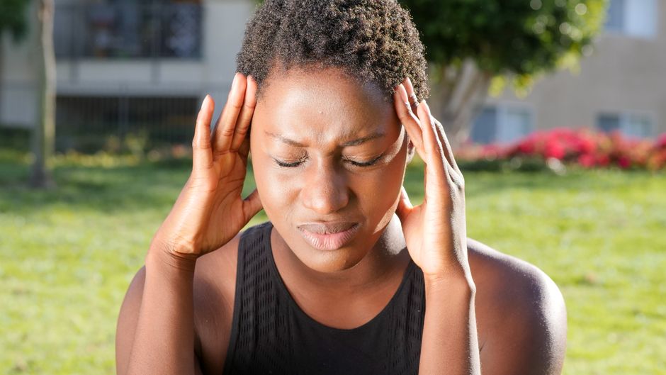 Dépression et maux de tête : ce que les études de 2025 mesurent A woman holding her head in pain, indicating a severe headache outdoors in a sunny setting.