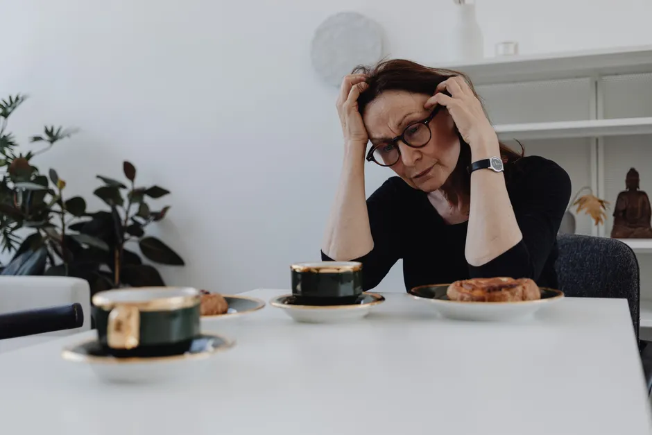 Perte d’appétit pendant le deuil : pourquoi manger devient si difficile A woman sits alone at a table, expressing sadness and grief in a quiet home setting.