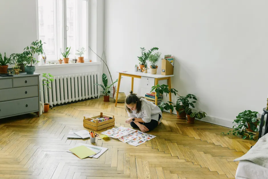 A young girl at home, deeply engrossed in art and craft activity on a wooden floor.