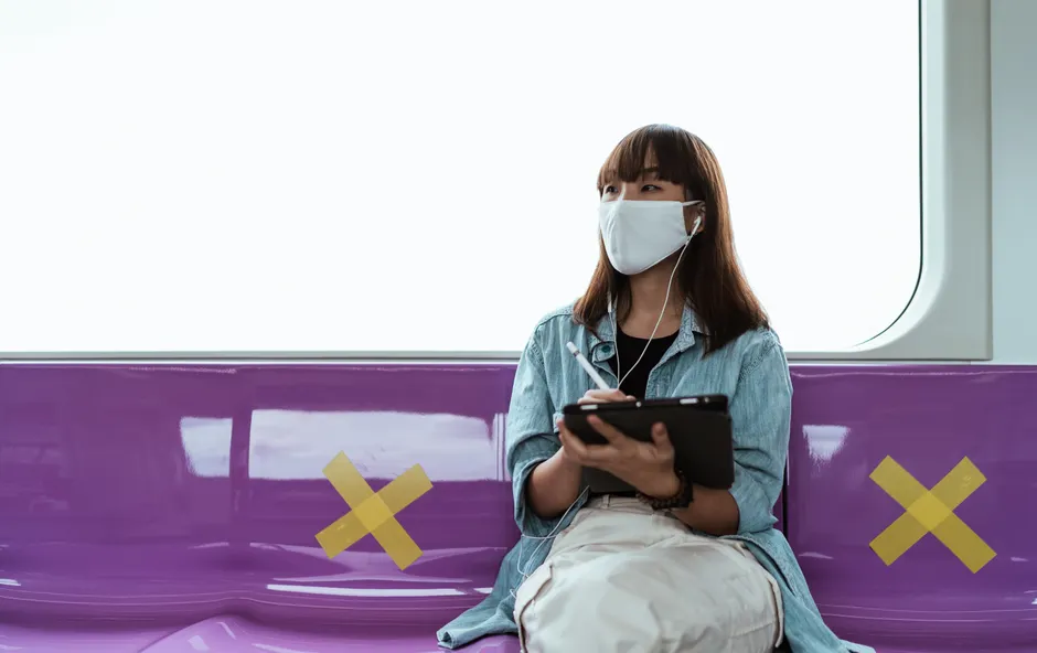 A young woman in a mask uses a tablet on a subway, adapting to public transport during the pandemic.