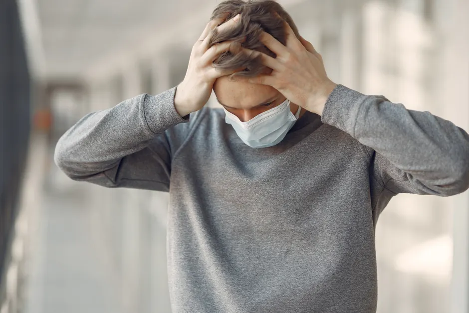 Adult male wearing a face mask, appearing stressed and worried while standing indoors.