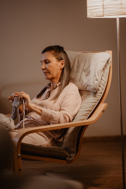 An adult woman peacefully crocheting in a cozy indoor setting, under soft lighting.
