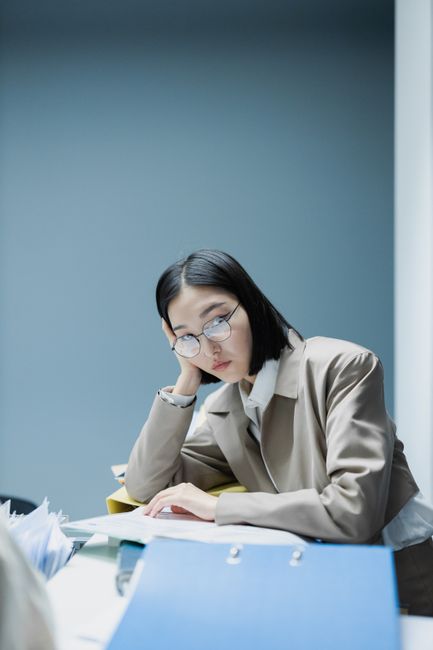 An Asian woman in glasses appears bored while working at an office desk.