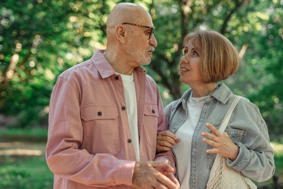 Comment savoir si l’on est amoureux? Distinguer le vertige du lien An elderly couple shares a joyful conversation in a vibrant green park setting.
