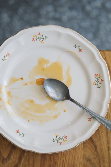 An ornate empty plate with a spoon on a wooden table, showing food remnants.