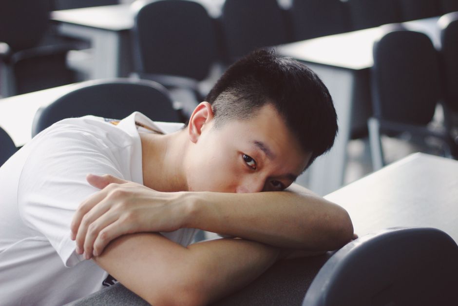 TDAH et introversion : quand le calme cache un cerveau en mouvement Asian man relaxing in a classroom, resting on a desk. Calm and peaceful atmosphere.