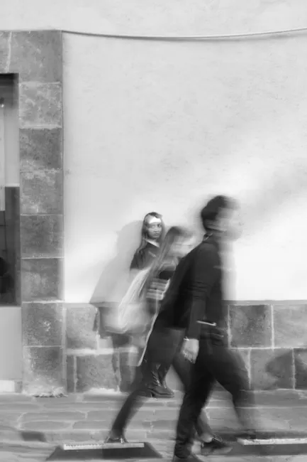 Black and white photo captures blurred motion of people walking past a stationary person on a city street