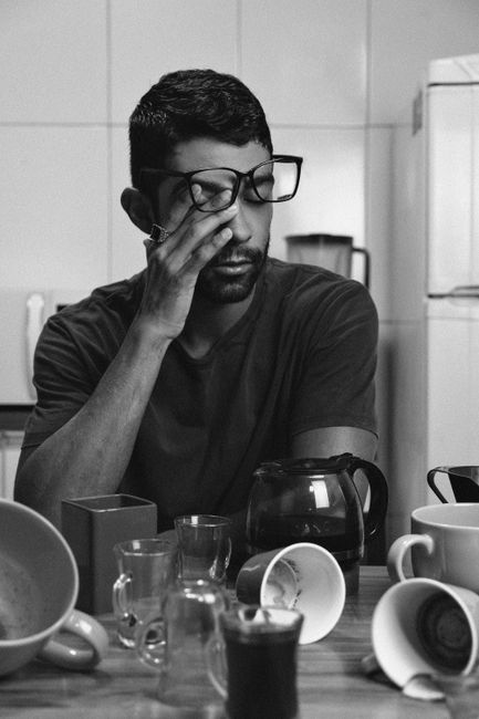 Black and white portrait of a tired man sitting at a kitchen table with coffee cups.