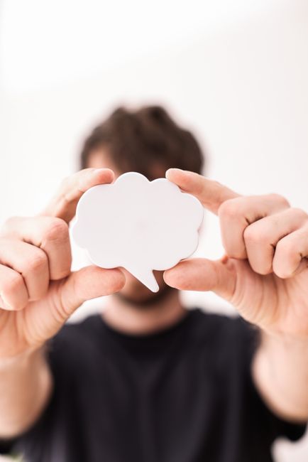 Blurry person holding a white speech bubble cutout in focus.