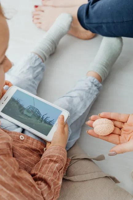 Child playing an educational game on a smartphone while holding a brain model.