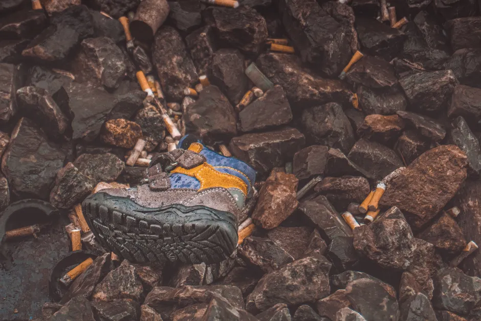 Child's shoe amidst cigarette litter and rocks; highlights pollution issue in Switzerland.