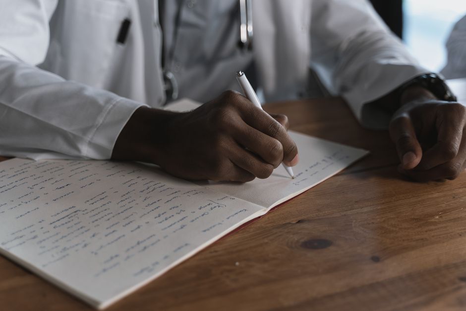 Récits de maladie : ce qu’ils révèlent de l’expérience psychologique Close-up of a doctor writing notes with a pen in a medical notebook on a wooden desk.