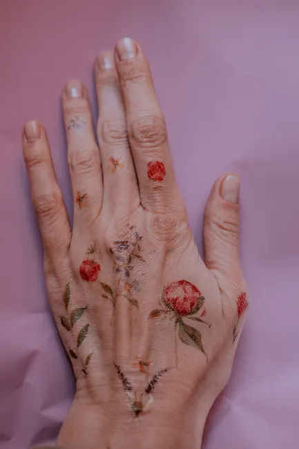 Close-up of a hand adorned with delicate floral temporary tattoos against a soft pink background.