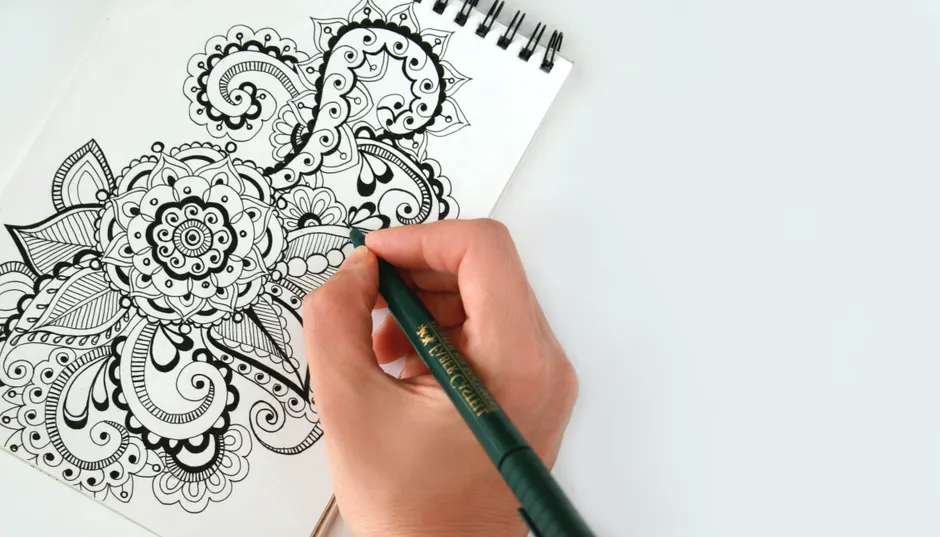 Zentangle et bien-être mental : ce que le dessin répétitif peut apporter Close-up of a hand drawing an intricate mandala pattern on a sketchbook using a pen. Perfect for creativity themes.