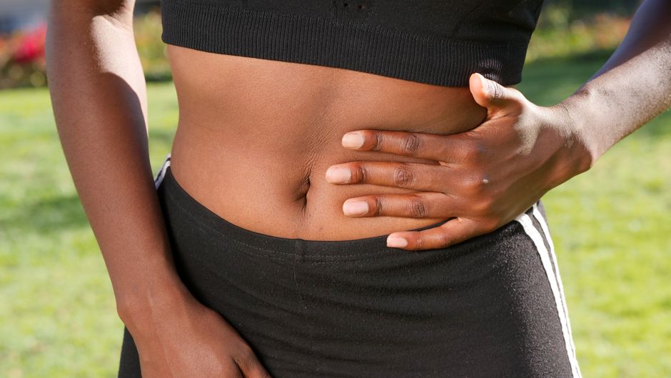 Migraine abdominale : reconnaître les crises et mieux les prendre en charge Close-up of a person holding their abdomen, indicating stomach discomfort, outdoors.