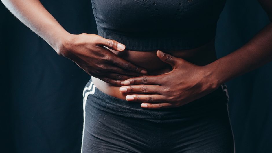 Anxiété et constipation : le lien cerveau-intestin, sans raccourci Close-up of a person pressing hands on abdomen, indicating discomfort or pain, against a black background.