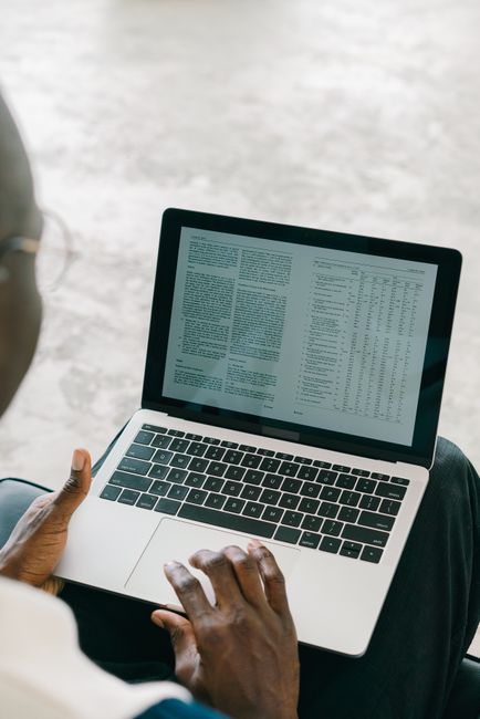 Close-up of a person using a laptop with spreadsheets and text on the screen.