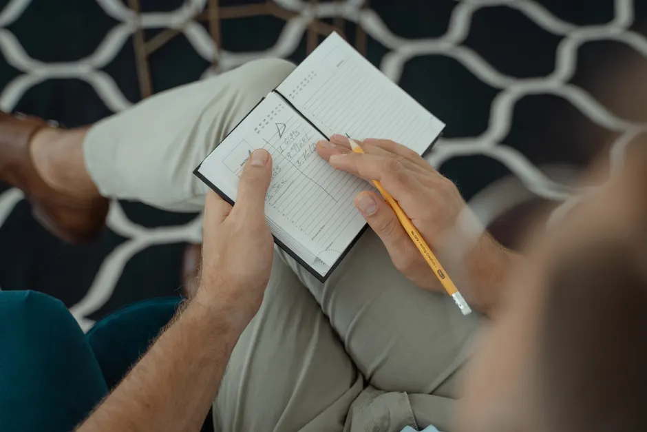 Close-up of a person writing notes in a notebook with a pencil, indoors.