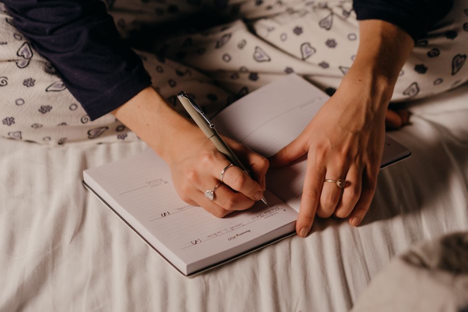 Close-up of a person's hands writing in a journal, showcasing a cozy nighttime ambiance.