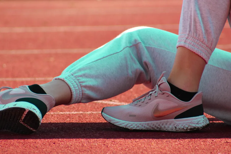 Résilience et passion : distinguer l’élan de la pression Close-up of athlete resting on track, showcasing pink sports shoes in warm sunlight.