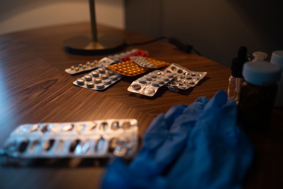Close-up of various medication blister packs and gloves on a wooden table, signifying health and recovery.