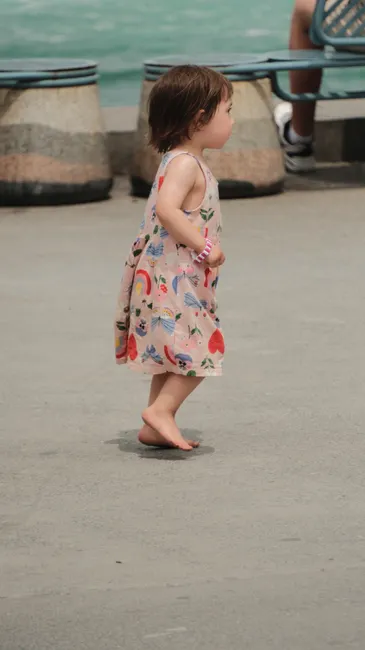 Cute toddler girl walking barefoot in a colorful dress outdoors by the sea.