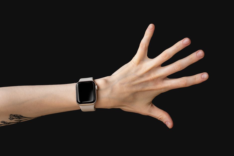 Elegant hand wearing a smartwatch with a tattooed wrist against a dark studio backdrop.