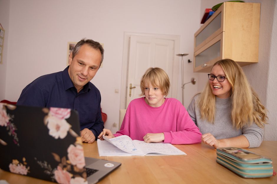 Family engaged in online learning together at home using laptop, focusing on education and connection.