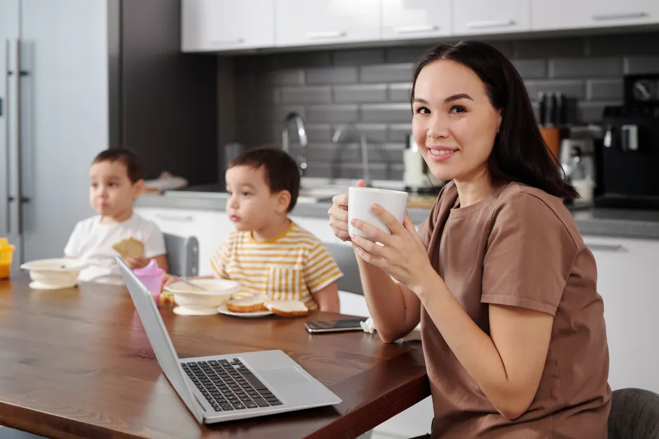 Mères qui travaillent : pourquoi le self-care ne suffit pas sans soutien Family enjoying breakfast in a modern kitchen. Woman holding coffee and smiling.